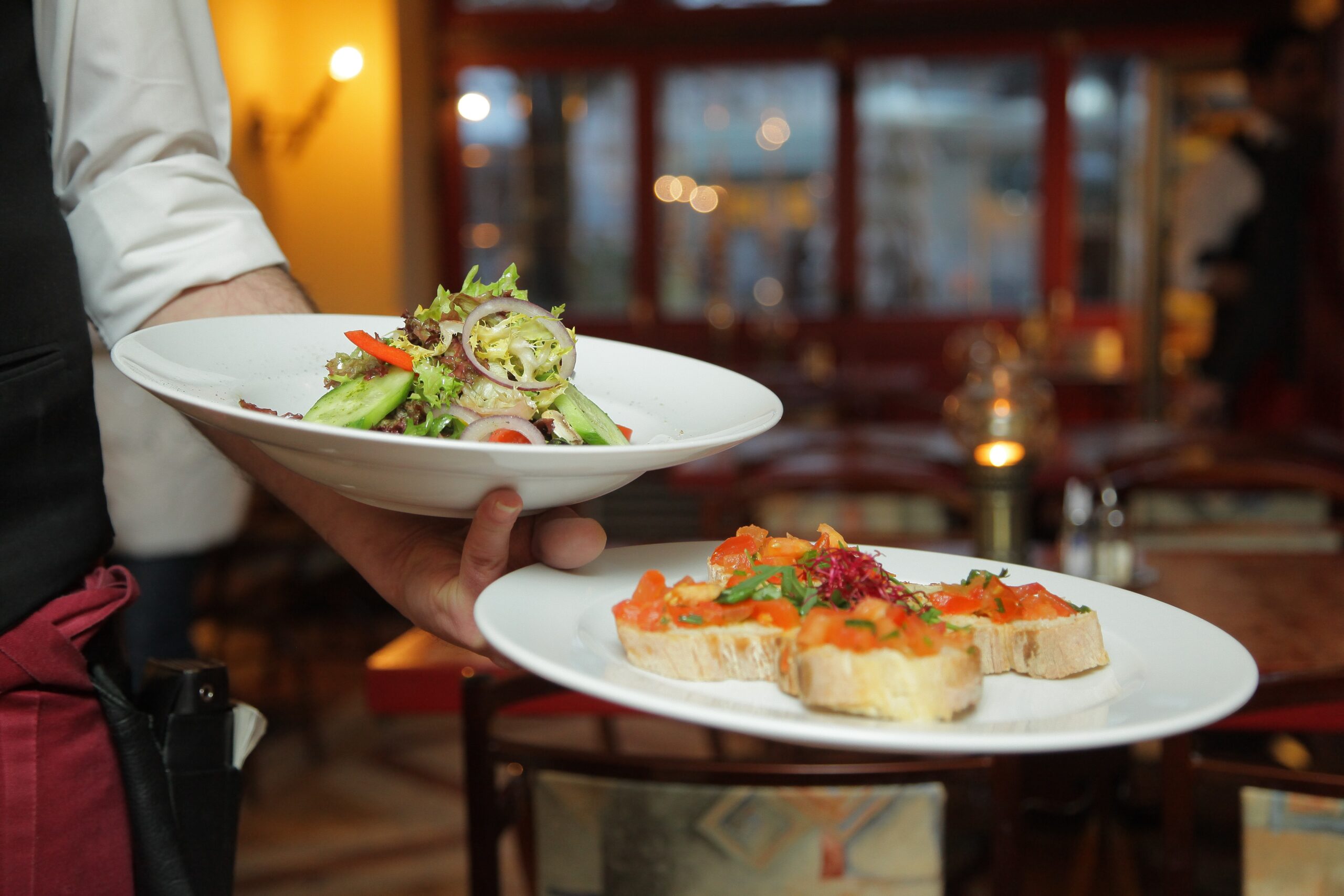 A server in Capitol Hill, Seattle, presenting a fresh salad and bruschetta at a cozy restaurant with warm lighting and elegant decor, highlighting the neighborhood's diverse dining scene.