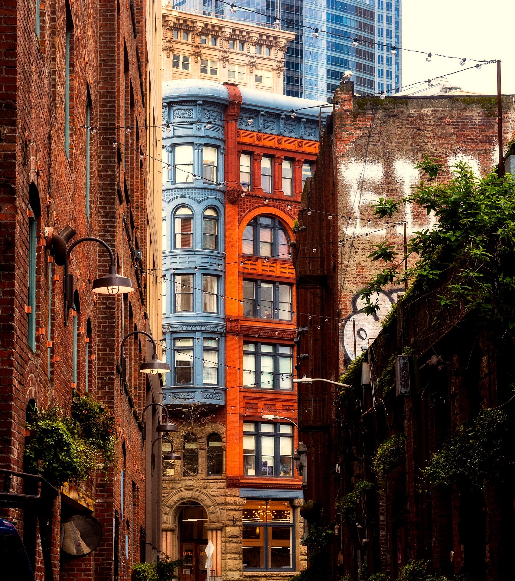 Historic red and blue building in Seattle’s Pioneer Square, viewed from a narrow brick alleyway with hanging lights.